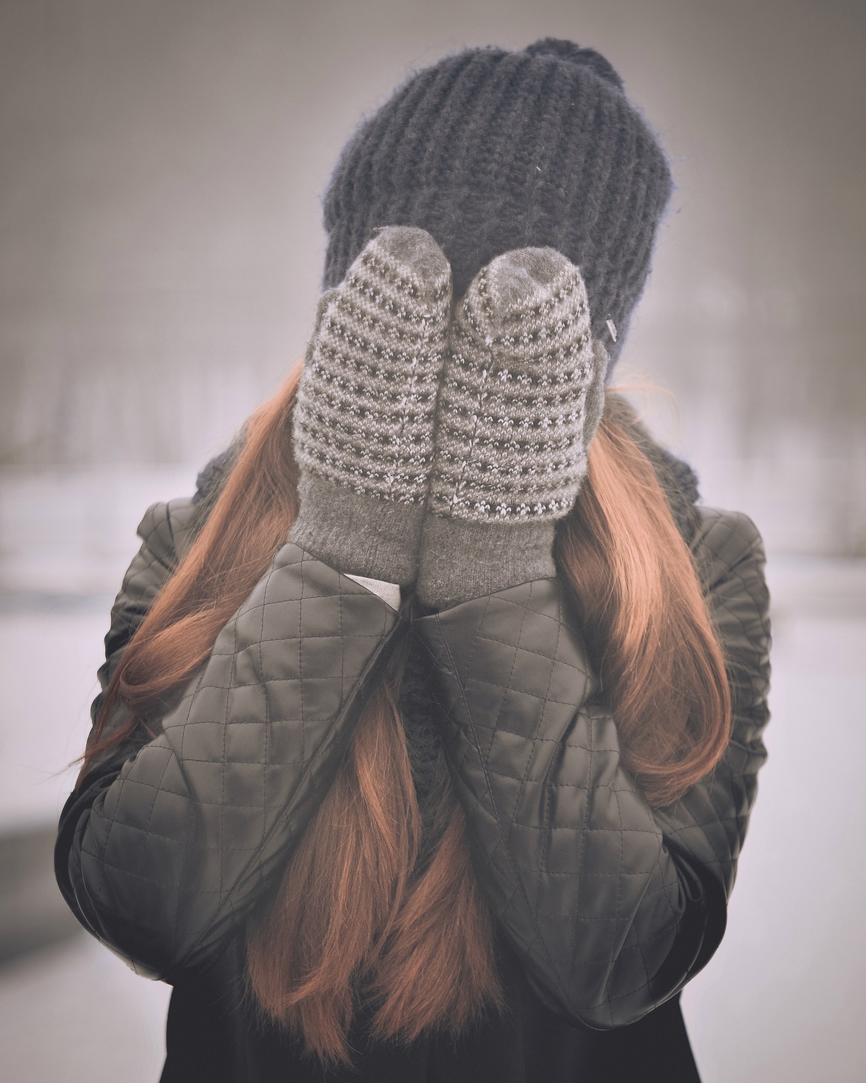 junge Frau in Winterkleidung bedeckt ihr Gesicht mit ihren Händen, die in Fäustlingen stecken.