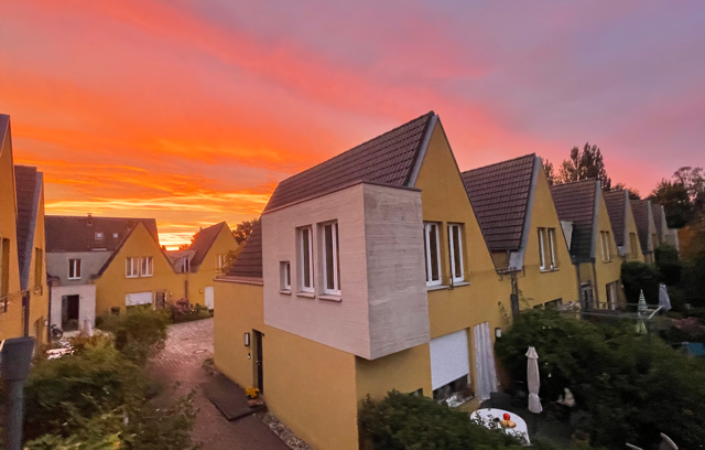 Gelbe zweistöckige Häuser vor rotglühendem Sonnenuntergang.